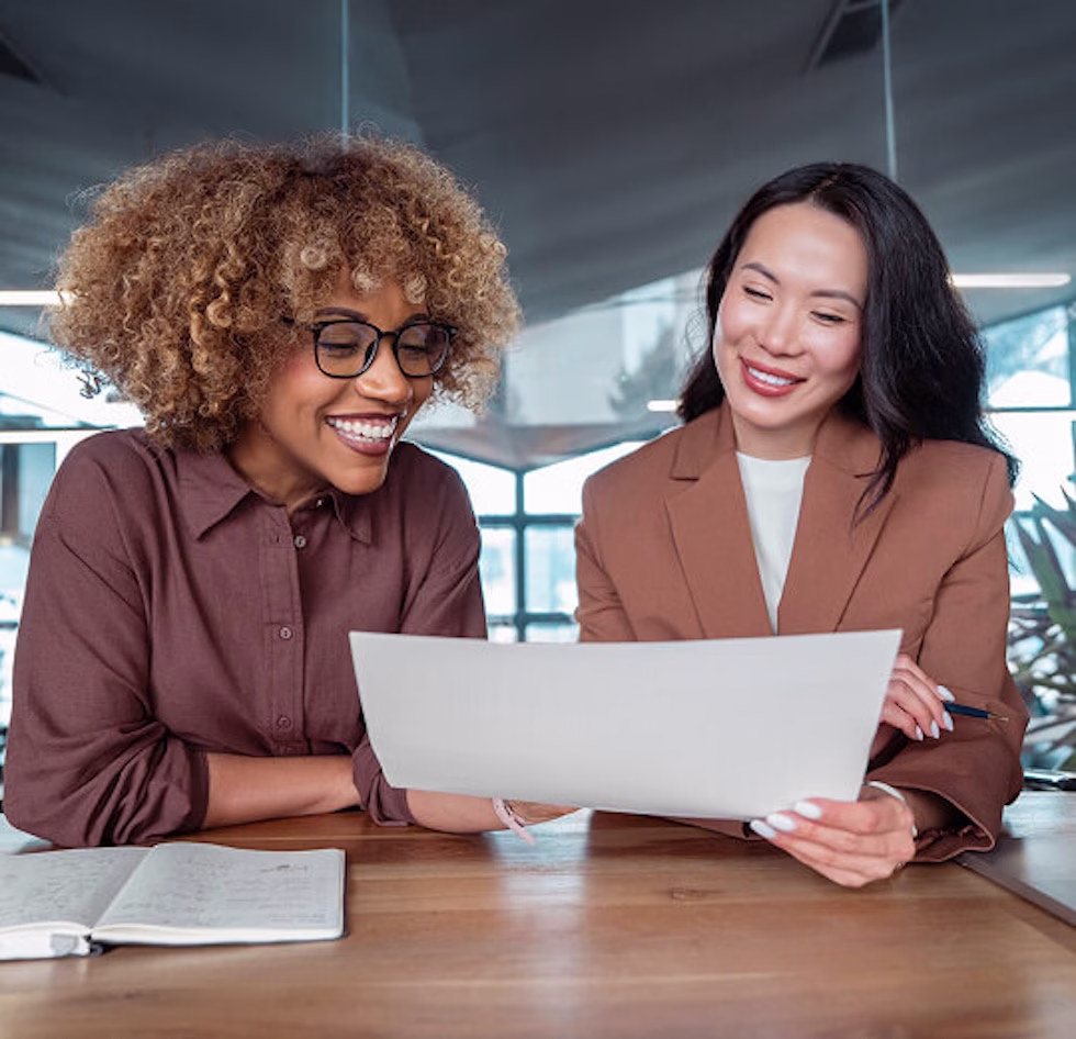 Two HR professionals smiling while reviewing an employee benefits benchmarking report at a table
